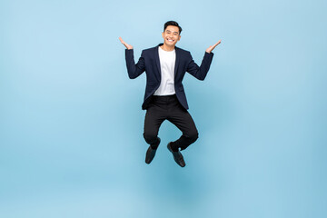 Full lenght portrait of happy Asian man jumping and smiling with open hands on isolated light blue studio background