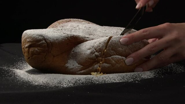 Man cutting a slice of Panettone. panettone cut with pieces of sugar on black background. Festive Christmas Italian dessert Panettone. Festive cooking, new year, delicious, sweets.
