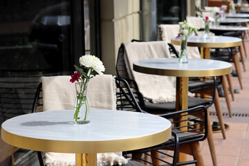 Street cafe with empty tables outdoor, city during coronavirus pandemic. Vases of flowers on a tables and vintage wooden chairs with warm plaids