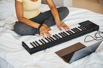 Female musician playing synthesizer and using notebook at home