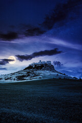 castle on the hill at night. composite fantasy landscape. grassy meadow in the foreground. rocky...
