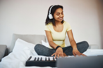 Cheerful young woman in headphones playing synth at home
