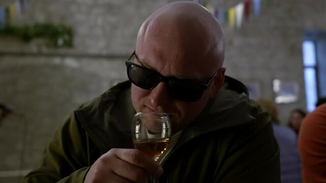 middle-aged man is tasting wine in cafe, sniffing, viewing color and drinking, portrait of male wine connoisseur