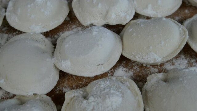 Rows of frozen raw pelmeni dumplings stuffed with mince meat on cutting board. Delicious traditional handmade food on domestic kitchen. Asian and russian cuisine. Dolly shot. Close-up.