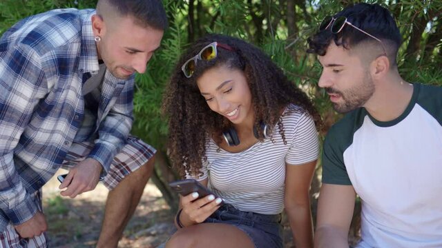 Multiracial young friends group sitting on city park bench having fun using smartphone with internet mobile connection technology. Hispanic beautiful curly girl chatting with phone on social network