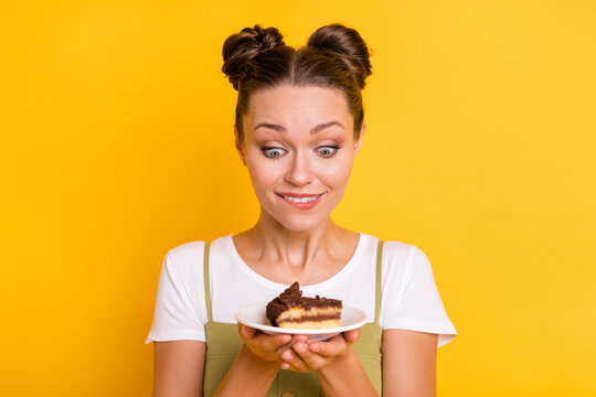 Photo of hungry excited adorable lady bite lip hold plate piece cake wear green overall isolated yellow background