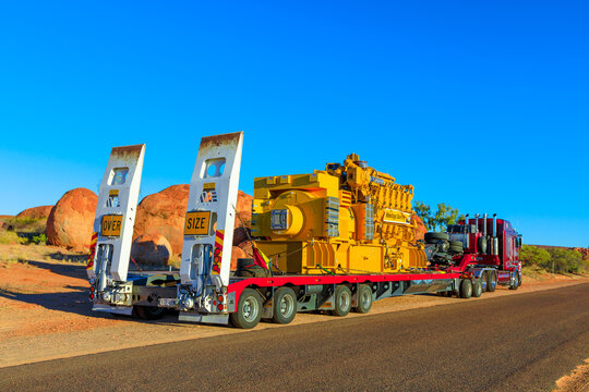 Northern Territory, Australia - August 12, 2019: red Kenworth truck of Clein Group crossing the Karlu Karlu, Devils Marbles Conservation Reserve in Northern Territory of Australian Outback at sunset.