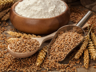 Still life with wheat, flour and spikelets in a spoon and bowl on an old table