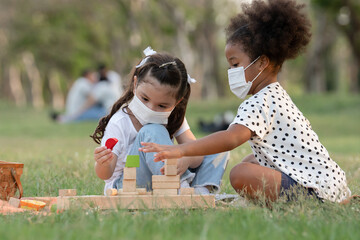 Couple little girls African and Caucasian kids wear face mask while sitting and playing wooden...