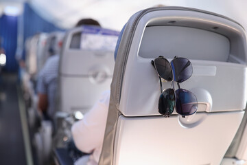 Two sunglasses hanging on back of passenger seat on airplane closeup