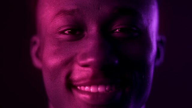 Close up portrait of happy young african american guy laughing at camera in purple neon lights, slow motion