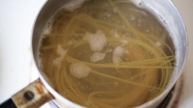 Long spaghetti are boiled in an iron pot. Water is boiling. Close-up
