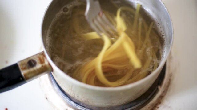 Long spaghetti are boiled in an iron pot. Water is boiling. Close-up