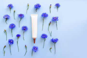 Moisturizer cream squeeze cosmetic tube with long nozzle and cornflower flowers on blue background...