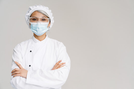 Asian woman in chef uniform and face mask standing with arms crossed