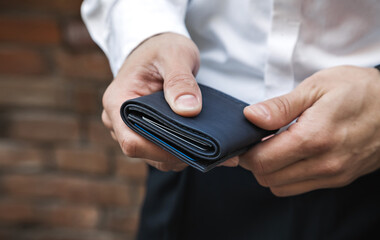 A businessman in a white shirt holds a wallet in his hands. Horizontal orientation, close-up, no face