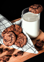 Cookies draped around a glass of milk, standing on a wooden board next to a checked cloth