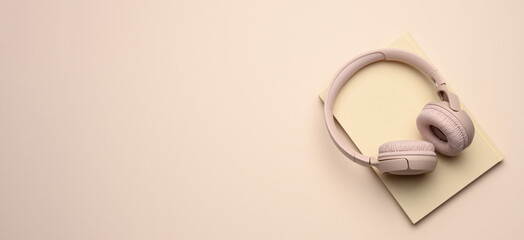 beige wireless headphones and a closed notepad on a beige background, banner