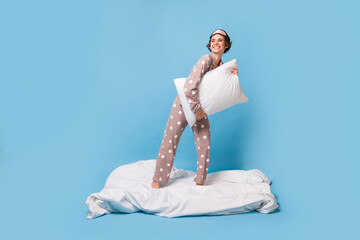 Full size photo of young happy positive cheerful girl in pajama and eye mask hold pillow isolated on blue color background