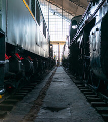 Vertical image of a road formed by two retro trains on its tracks. At the end of the road is a large window and a young woman.