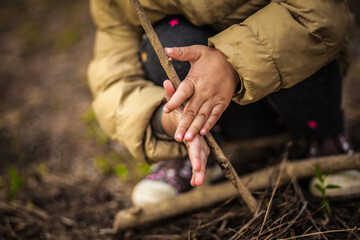 a child on a hike in a puffed brown jacket learns to make fire with a stick