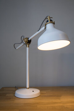 Closeup Of A Lit White Table Lamp On A Wooden Table