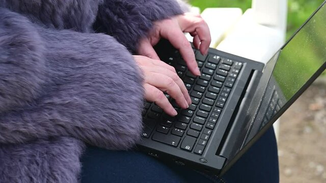 Frau in einer Kaninchenfell Jacke arbeitet im Garten mit einem Notebook im Homeoffice  