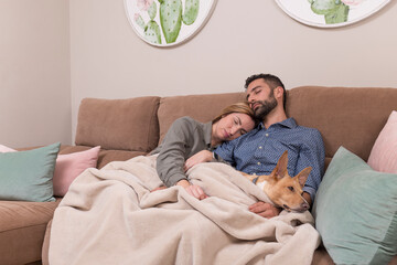 couple and their dog asleep, the man, the woman and the dog have fallen asleep sitting on a brown sofa and covered with a blanket
