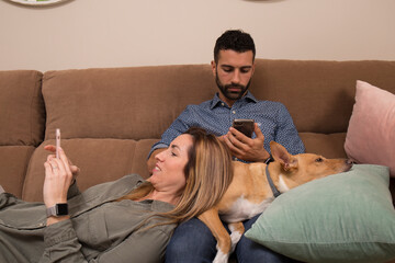 couple sending messages on the mobile, young couple with their dog lying on the sofa write with their mobile