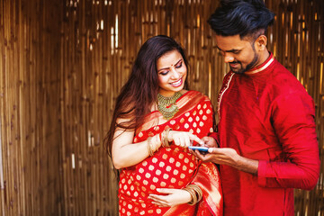 Happy pregnant Indian woman with her husband choosing doctor online. Happy couple using phone together