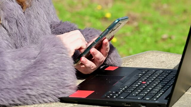 Frau in einer Kaninchenfell Jacke arbeitet im Garten mit einem Notebook im Homeoffice  