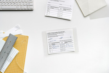 Obraz premium Fake covid vaccination record card. Covid scams. Forged health certificate with false vaccination record against covid-19. Blank card, pen, paper knife,laminator. Top view, flat lay on white table.