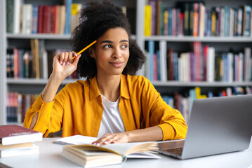 Pensive african american female student, stylishly dressed, with curly hair, sits at a table,...