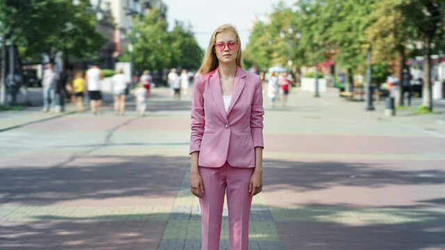 Zoom-in time lapse of attractive lady wearing elegant clothing and sunglasses standing in busy street among crowd op people on summer day. Youth and lifestyle concept.