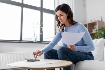 accounting, taxes and finances concept - young woman with papers and calculator at home