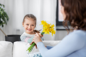 people, family and holidays concept - happy little daughter giving daffodil flowers to mother at...