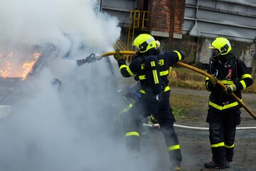 Firefighters with breathing apparatus extinguish a car that is completely engulfed in fire