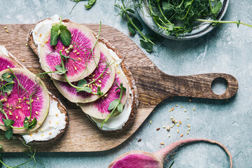 Watermelon radish toast with cream cheese and micro-green peas on a serving board.