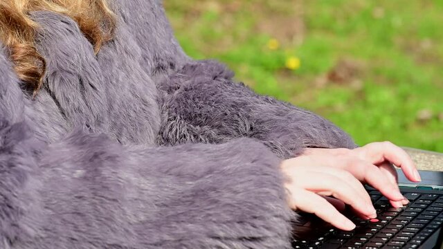 Frau in einer Kaninchenfell Jacke arbeitet im Garten mit einem Notebook im Homeoffice  