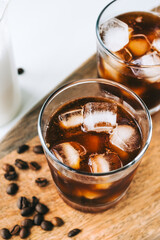 Ice coffee americano in glass with ice cubes on wooden board, close-up.