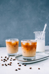 Ice coffee in glass with milk foam and ice cubes, coffee beans on white table.