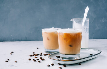 Ice coffee in glass with milk foam and ice cubes, coffee beans on white table.