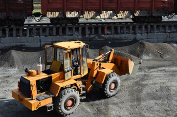 Wheel loader unloading bulk cargo from freight cars  at a cargo railway station. Fron-end loader unloads crushed stone from gravel pit. Gravel  a cement production site.