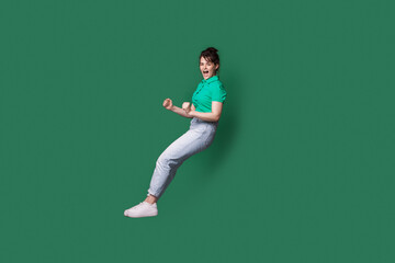 Fototapeta na wymiar Caucasian woman is jumping on a green studio wall screaming while advertising something