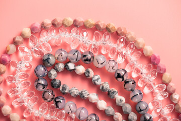 Faceted and smooth round beads made of quartz and natural stone on threads on a pink background. Top view - 429176749
