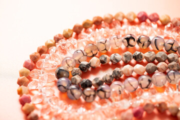 Faceted and smooth round beads made of quartz and natural stone on threads on a pink background - 429176750