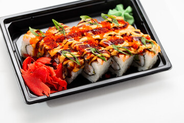 Asian rice and fresh fish rolls with hot sauce garnished with sliced onions and red fish roe. Stock image of food from a delivery service on a plastic tray