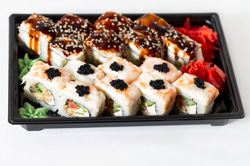 Home delivery of Asian food. Rice rolls with shrimp meat, eel and creamy white cheese garnished with sauces, on a black plastic tray