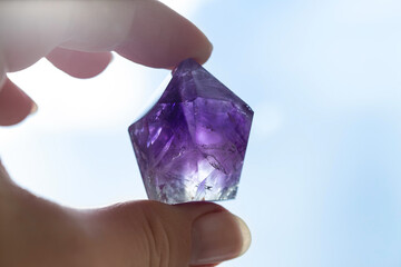 Transparent amethyst crystal in hand, close-up shot. Purple beautiful semi-precious faceted stone