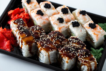 Rice square rolls with shrimp, eel, vegetables, creamy white cheese and sweet sauce. Asian sushi of two types on a plastic tray